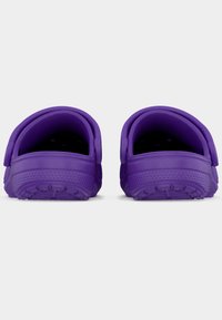 Ζευγάρι μοβ λαστιχένιων τσόκων, εμφανιζόμενο από πίσω, με υφή στα πέλματα και ρυθμιζόμενα λουριά τακουνιού σε λευκό φόντο.