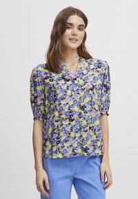 Blusa floreale nei colori viola, blu, giallo e verde. Presenta un colletto, maniche corte a sbuffo e una vestibilità comoda. Tessuto morbido con un motivo vivace.