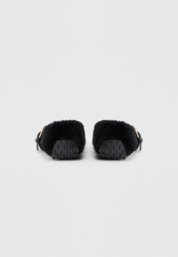 Sorte slippers med en blød, tekstureret overdel og gummisål. Har en afrundet form med et lille sort rem og guld hardware detaljer.