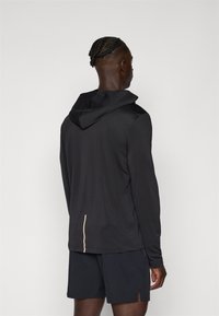 Felpa performance nera a maniche lunghe con una finitura testurizzata e un accento dorato sulla schiena. Abbinata a pantaloni corti neri coordinati.