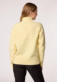 Geel, geribbelde coltrui van zacht materiaal, met een ontspannen pasvorm en lange mouwen, gecombineerd met donkere broeken.