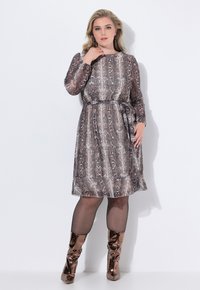 Braunes Schlangenmuster-Kleid mit langen Ärmeln, taillierter Taille und einer Schleifendetail. Getragen mit glänzenden bronze-farbenen Stiefeln bis zum Knie. Weiche Textur.