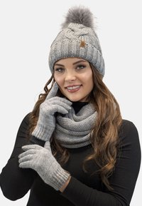 Grå strikket hue med en pom-pom, matchende tørklæde og handsker. Har ribbet tekstur og en glat overflade, velegnet til koldt vejr.
