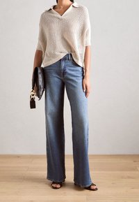 Jasnobeżowy dzianinowy sweter polo z krótkimi rękawami, zestawiony z niebieskimi dżinsami o wysokim stanie i szerokich nogawkach. Czarna kopertówka i sandały.