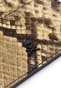 Material con estampado de serpiente texturizado en tonos marrón y beige, con un acento de calavera negra y huesos cruzados. Acabado brillante y bordes cosidos.
