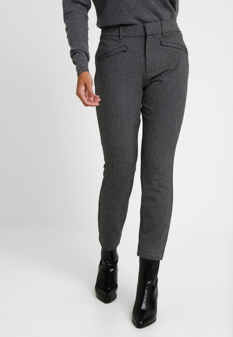 Personne portant un pantalon ajusté texturé gris foncé et des bottines noires pointues, avec un pull gris foncé assorti visible.
