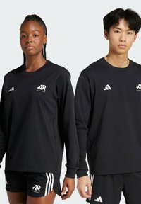 T-shirts de sport noirs à manches longues avec des logos blancs. Une paire de modèles ; l'un portant un t-shirt avec des shorts, l'autre avec un pantalon. Tissu doux et lisse.