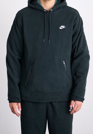 Sort Nike fleece-hættetrøje med front-kængurulomme med to lodrette lynlåse, båret over matchende sorte Nike bukser.