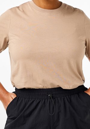 Beige T-shirt met korte mouwen en een ronde hals, gemaakt van zachte stof. Gecombineerd met een zwarte broek met een ingesloten tailleband en trekkoord.