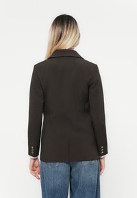 Brun skreddersydd blazer med klipp krage, lange ermer og knappdetaljer på mansjettene, sammen med lyseblå høytlivsjeans.