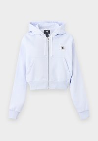 Sudadera corta de color azul claro con cremallera frontal, dos bolsillos laterales y un parche de logo circular en el lado izquierdo del pecho. Textura suave y puños acanalados.