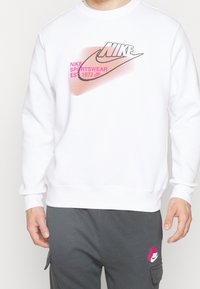 Vit Nike sweatshirt med en grafisk logotyp i svart och rosa, med avslappnad passform och ribbade ärmslut och nederkant.