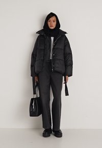 Casaco puffer preto com um design acolchoado, combinado com jeans escuros e sapatos pretos robustos. Acessorizado com uma bolsa preta e um hoodie.