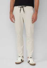 Lichtbeige cargo-broek met zwarte trekkoord, tapered fit, twee zijzakken en een gladde textuur, gecombineerd met witte sneakers.