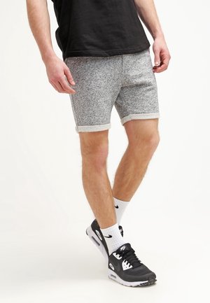 Grijze, gestructureerde shorts met een lichte stretch, omgeslagen zoom en zijzakken. Gecombineerd met zwarte sportschoenen en witte sokken.