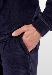 Granatowy, prążkowany zestaw ubrań do noszenia w domu zbliżenie na dłoń w kieszeni, ukazujące fakturę i elastyczny mankiet.