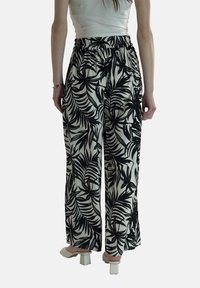 Zwart-witte wijde broek met een elastische tailleband, versierd met een palmbladerenpatroon. De stof lijkt lichtgewicht en soepel.