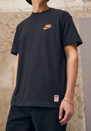 Sort bomulds-T-shirt med orange Nike-logo på brystet og en syet label på kanten. Afslappet pasform med korte ærmer.