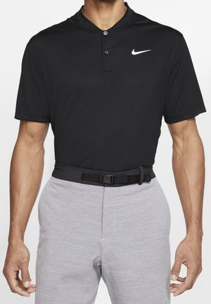 Mann trägt ein schwarzes Nike-Poloshirt mit kurzen Ärmeln und zwei Knöpfen, kombiniert mit hellgrauer Hose und einem schwarzen Gürtel mit rechteckiger Schnalle.