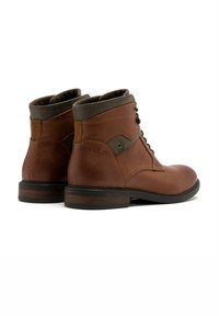 Brązowe skórzane botki za kostkę o fakturowanym wykończeniu, z sznurówkami z przodu, zielonymi akcentami oraz niskim, solidnym drewnianym obcasem.