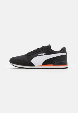 Zapatilla Puma en blanco y negro con acento naranja en la suela, diseño con cordones y logo de Puma en el lateral y el talón.