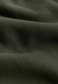 Tissu vert foncé avec une texture douce et lisse, présenté en gros plan, mettant en valeur les plis délicats et les détails fins du tricot.
