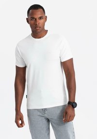 Bílý bavlněný tričko s kulatým výstřihem a krátkým rukávem, s malým logem na hrudi, spárované se světle šedými džíny.