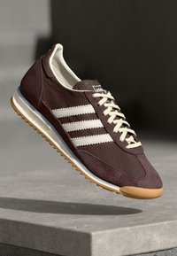 Scarpa sportiva bordeaux con tre strisce bianche, materiali in suede e rete, design con lacci, suola in gomma con superficie antiscivolo e branding classico.