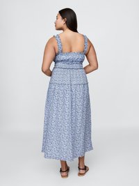 Blå floral maxi-kjole med smocket midje, brede stropper og lagdelt skjørt. Stoffet er lett, med en myk tekstur og et flytende design.