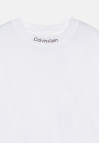 Vit bomullströja med rund halsringning. Har en Calvin Klein-logotyp i beige broderad på kragen. Slät struktur, utan mönster.