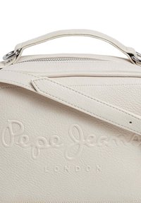 Bolso de mano de piel crema con el logotipo en relieve "Pepe Jeans London", que cuenta con un asa superior y acentos de hardware en plata. Cierre de cremallera en la parte superior.