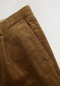Pantaloni din corduroy maro cu o textură cu nervuri și un tiv ajustat, prezentând caneluri verticale și cusături curate de-a lungul cusăturilor.