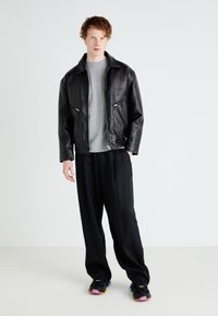 Black leather jacket with a zip, gray sweater underneath, black loose-fitting pants, and colorful-soled black sneakers.