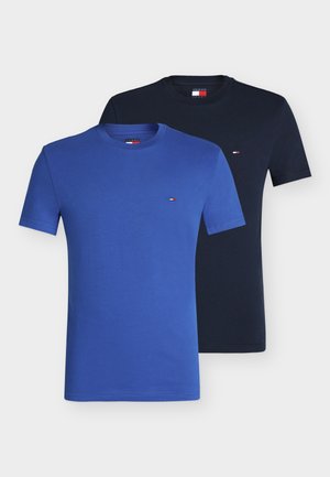 Dos camisetas lisas con cuello redondo, una azul real y una negra, cada una con un pequeño logotipo rojo, blanco y azul en el pecho.