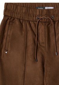 Pantaloni in morbido tessuto marrone con vita elastica, regolazione con cordino, due Tasche laterali e sottili accenti metallici. Etichetta del marchio visibile.