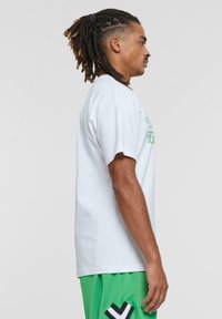 Hvid bomulds t-shirt med løs pasform, prydet med grøn tekst. Sammen med grønne mesh shorts, der viser et kontrasterende sort designelement.