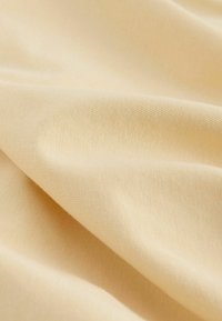 Tissu beige doux avec une texture fine en tricot, délicatement plié pour montrer une surface lisse et des ombres subtiles.