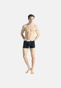 Boxer shorts neri con una cintura elastica bianca caratterizzata da tre strisce nere. Il tessuto ha una texture liscia e un design aderente.