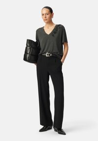 T-shirt gris à col en V avec des embellissements floraux, pantalon noir taille haute, et un sac noir en forme de coussin. Tissu texturé et formes épurées.