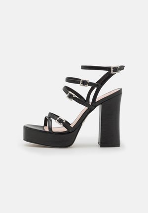 Black platform heels with thick block heel, multiple adjustable straps, and silver buckles. Smooth leather upper and textured sole.