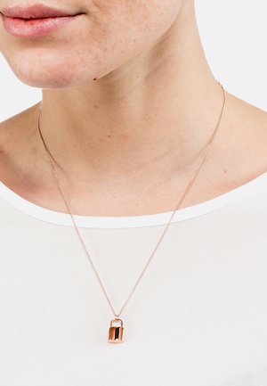 Roségoldene Halskette mit einem Vorhängeschloss-Anhänger, feiner Kette und glatter Oberfläche, getragen über einem weißen Oberteil mit rundem Ausschnitt.