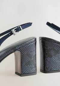 Tumedad sandaalid, millel on roomaja tekstuuriga viimistlus, peened rihmad ja metallist äärisega pandla; plokknina stabiilsuse tagamiseks.