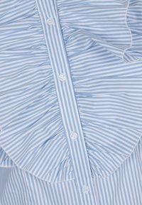 Niebiesko-biała bluzka w paski z pionowymi pasami, falbaniastym kołnierzykiem i białymi guzikami z przodu, o miękkiej fakturze materiału.