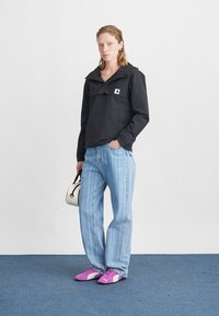 Schwarze Jacke mit Kapuze, Vordertasche; hellblaue gestreifte weite Jeans; pinke Sneaker; kleine weiße Handtasche mit schwarzen Akzenten.