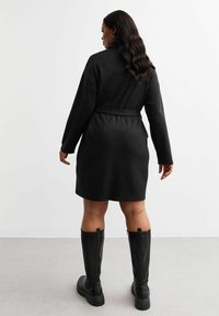 Svart klänning med bälte, långärmad design och mjukt material. Kombinerad med svarta knähöga stövlar och en slät finish.