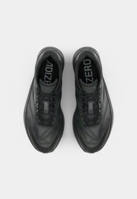 Chaussures de sport noires avec une tige en mesh texturé, présentant des accents verts et une semelle rembourrée. Les lacets et les détails de marque sont visibles.