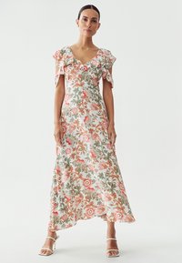 Robe maxi florale avec des manches courtes évasées, pr�ésentant une base blanche, des motifs floraux roses et verts, et une silhouette fluide.