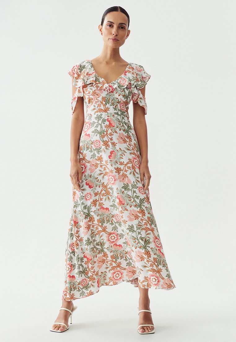 Robe maxi florale avec des manches courtes évasées, présentant une base blanche, des motifs floraux roses et verts, et une silhouette fluide.