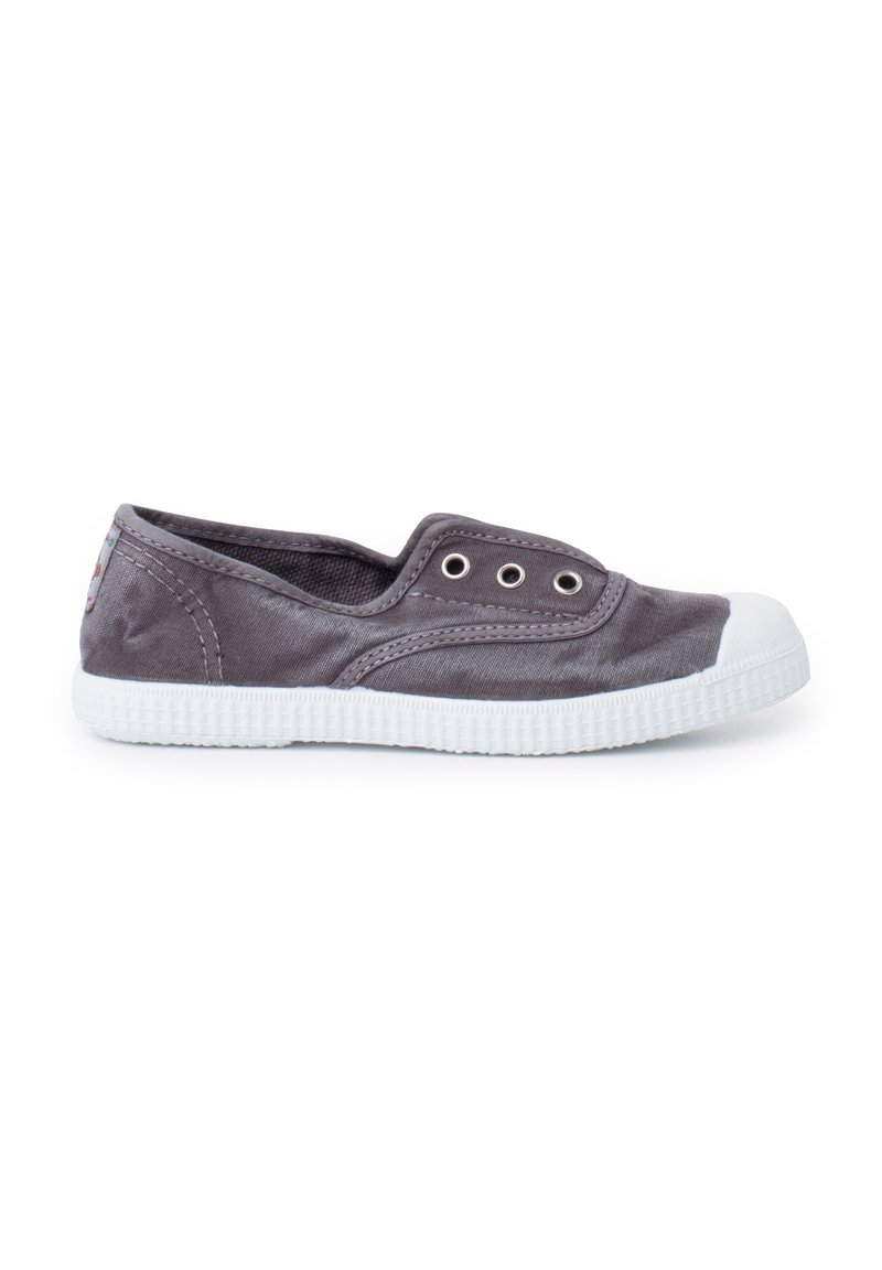 Zapato slip-on de lona gris con suela de goma blanca y punta reforzada. Presenta ojales en los lados y un revestimiento texturizado para mayor agarre.