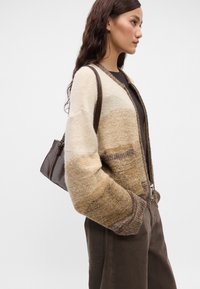 Πλεκτό καρδιόνι σε καφέ και μπεζ αποχρώσεις με άνετη εφαρμογή, διαθέτει φερμουάρ, πλαϊνές τσέπες και αντίθετες υφασμάτινες μανσέτες.